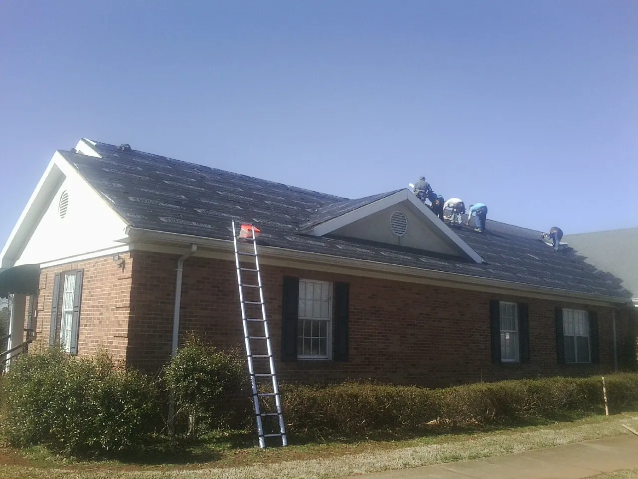 Crew tearing shingles off a brick ranch roof with a ladder set — Emergency Roof Repair work by our crew in Sandy Level