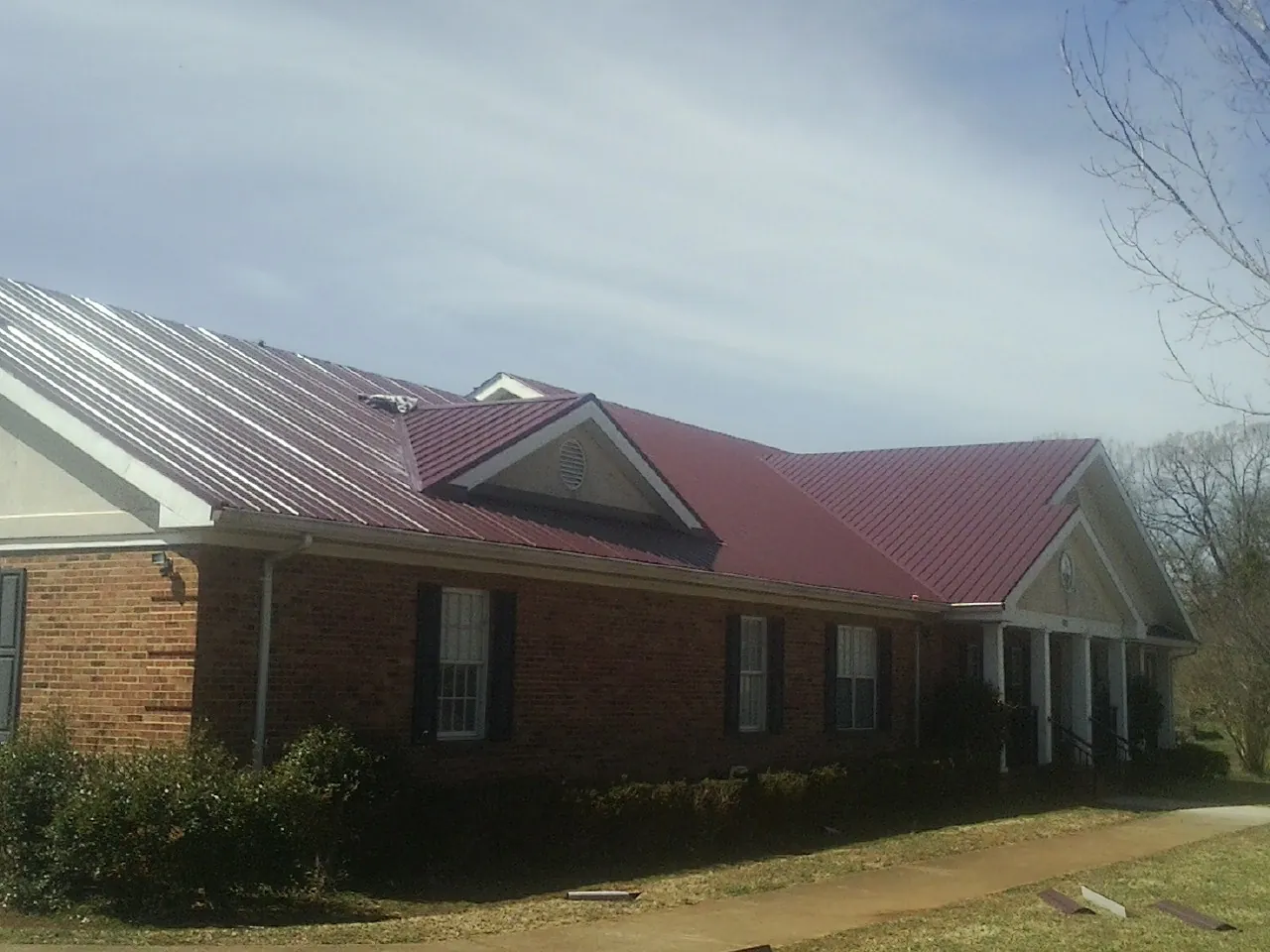 Red metal roof with gabled entries on a long brick building, from a Hail Damage Roof Repair job in Sandy Level