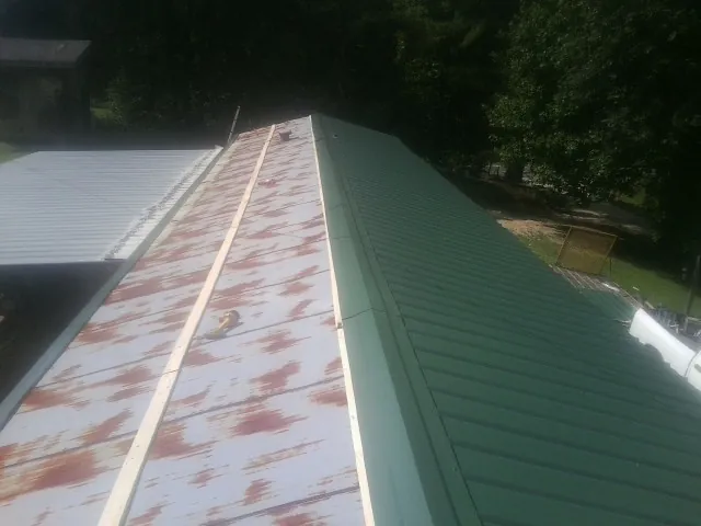 Old rusted panels beside newly installed green metal roofing — Wind Damage Roof Repair by Roofing Brothers in Sandy Level