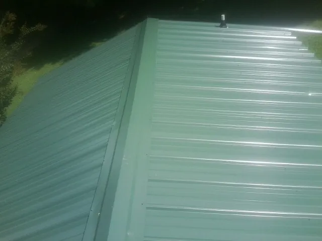 New green metal panels meeting at the ridge of a roof — Flat Roof Repair work by our crew in Sandy Level