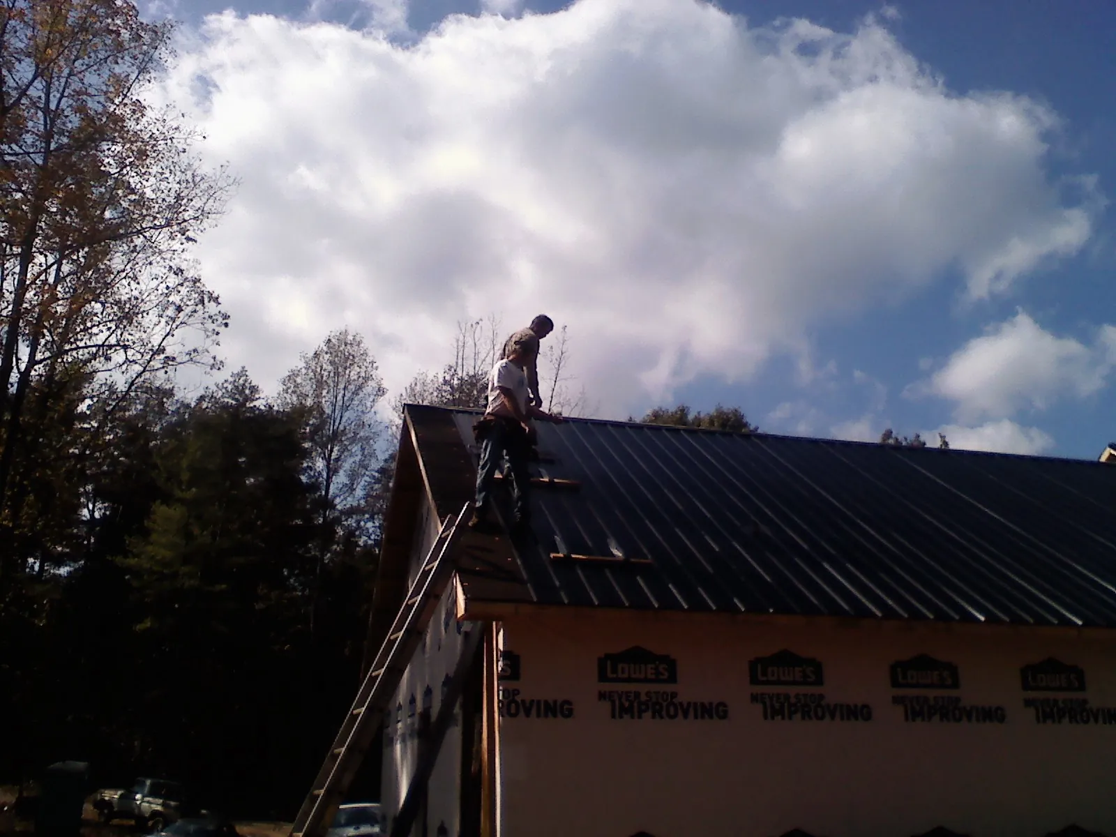 Roofer fastening dark metal panels high against a cloudy sky, from a Roof Inspection job in Sandy Level