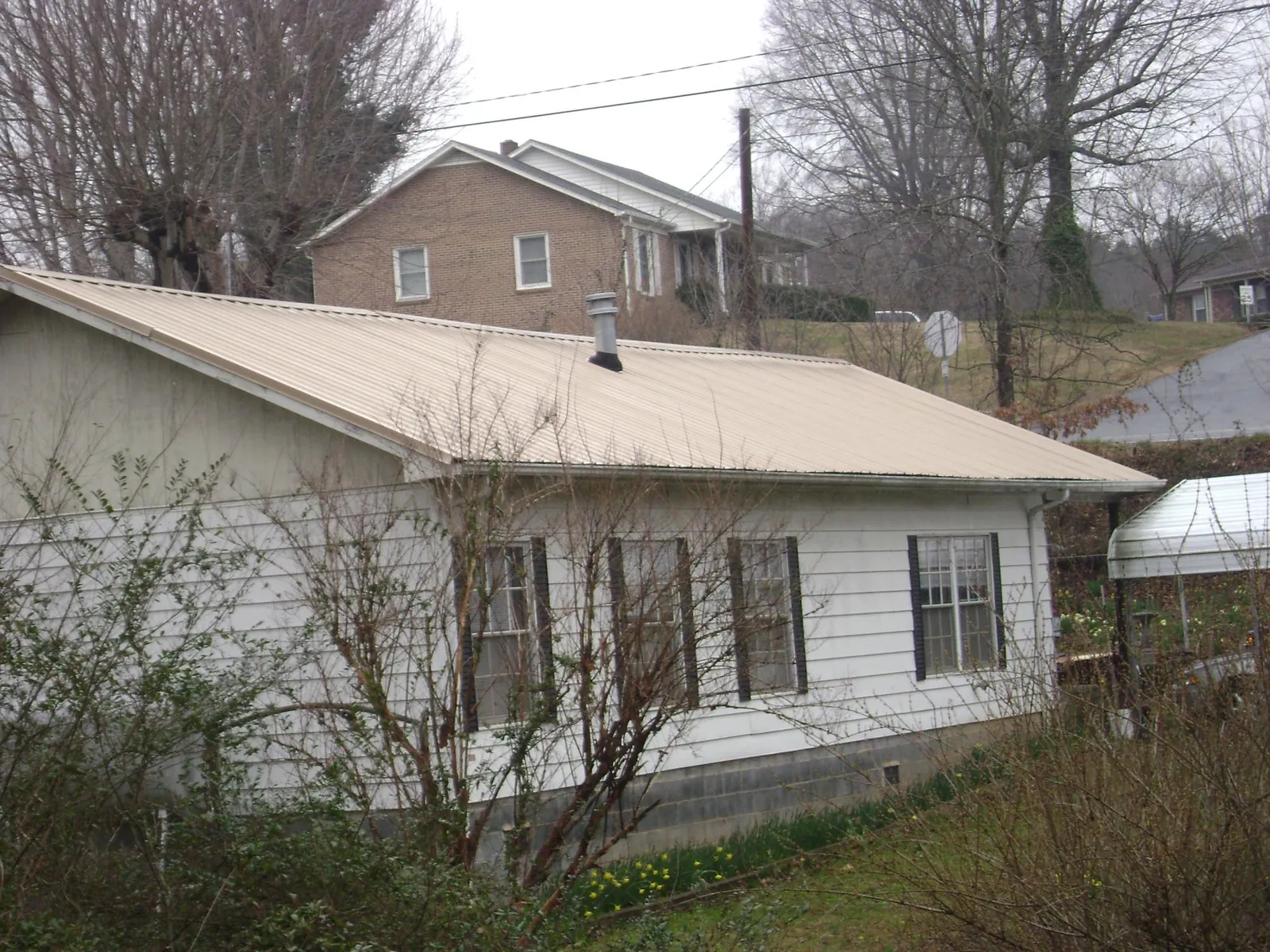 Tan metal roof on a white sided house set into a hillside — Commercial Roofing by Roofing Brothers in Sandy Level